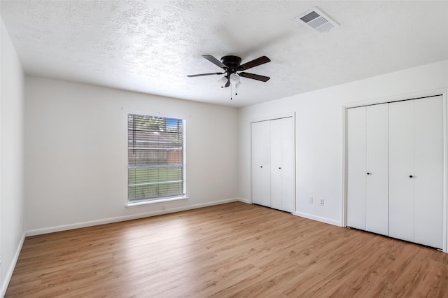 unfurnished bedroom featuring multiple closets, ceiling fan, a textured ceiling, and light wood-type flooring