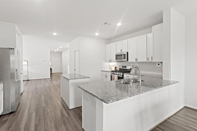 kitchen with kitchen peninsula, appliances with stainless steel finishes, light stone countertops, and white cabinets