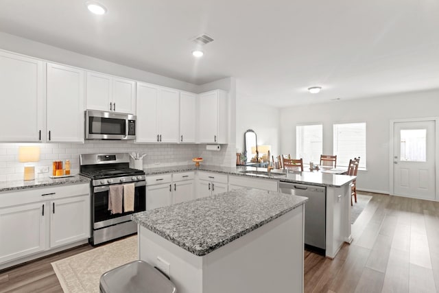 kitchen with white cabinetry, stainless steel appliances, a center island, and kitchen peninsula