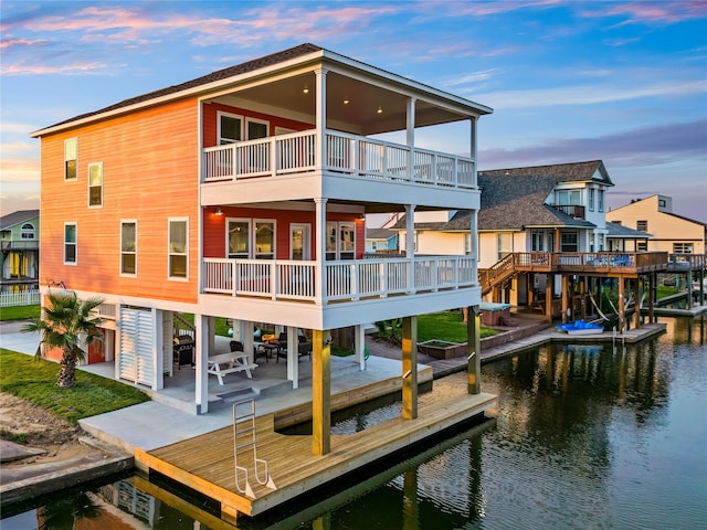 back house at dusk with a deck with water view and a patio area