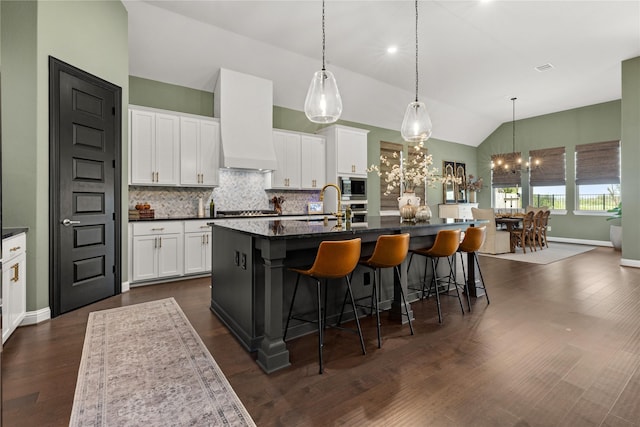 kitchen with white cabinets, vaulted ceiling, a kitchen island with sink, and premium range hood