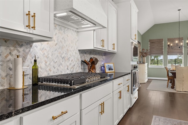 kitchen featuring vaulted ceiling, appliances with stainless steel finishes, white cabinetry, dark stone countertops, and custom range hood