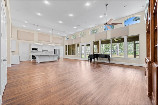 unfurnished living room featuring a towering ceiling, ceiling fan, plenty of natural light, and light wood-type flooring