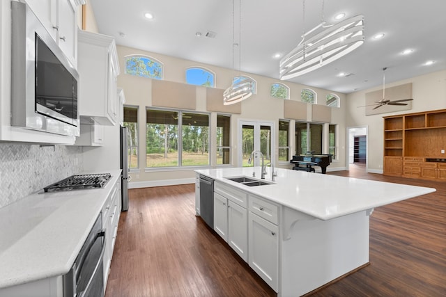 kitchen with an island with sink, sink, white cabinetry, stainless steel appliances, and ceiling fan with notable chandelier