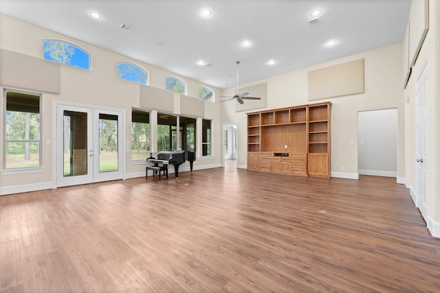 unfurnished living room featuring a high ceiling, ceiling fan, hardwood / wood-style flooring, and french doors