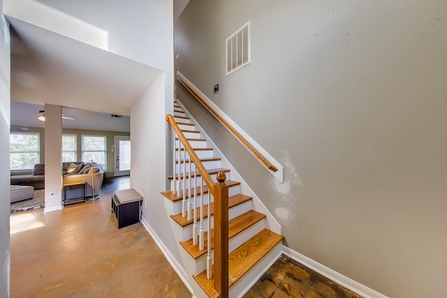 stairs with ceiling fan and concrete flooring