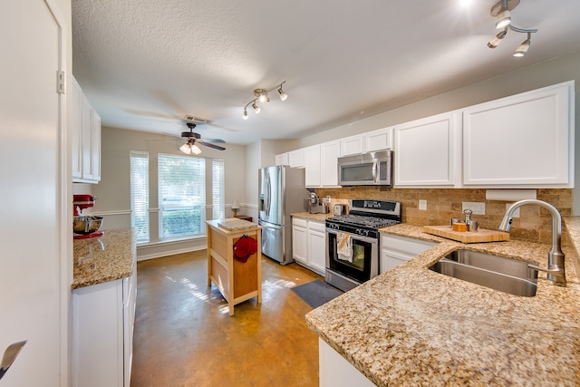 kitchen featuring sink, white cabinets, decorative backsplash, stainless steel appliances, and ceiling fan