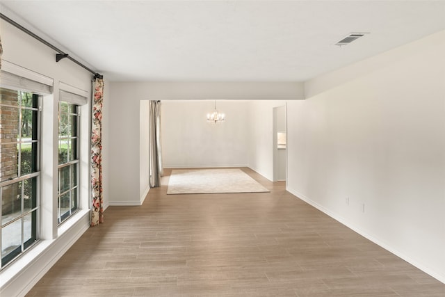 empty room featuring an inviting chandelier and light hardwood / wood-style flooring