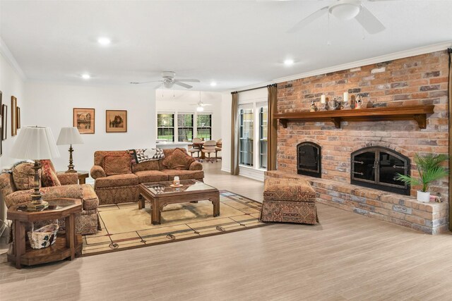 living room featuring ceiling fan, a fireplace, light wood-type flooring, and crown molding