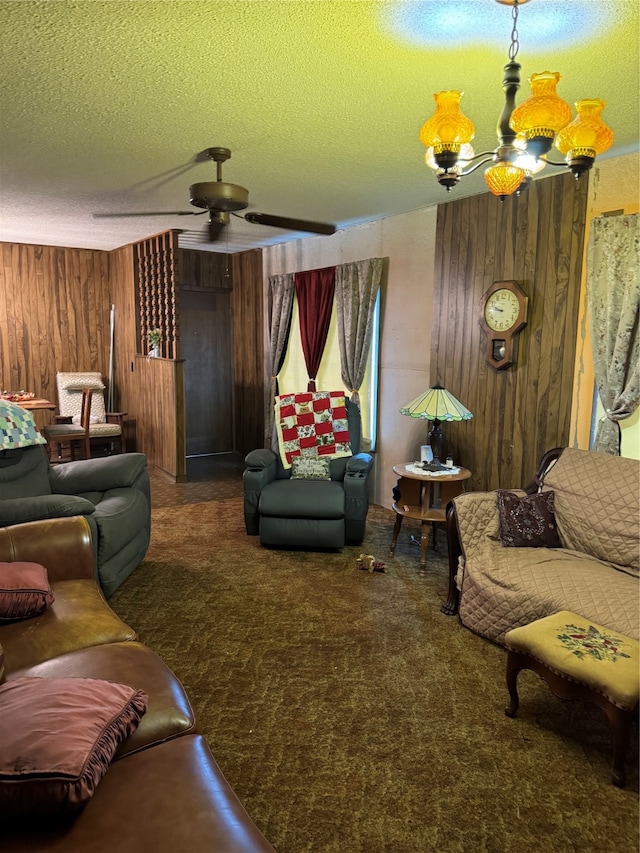 living room featuring a textured ceiling, ceiling fan with notable chandelier, wood walls, and dark colored carpet