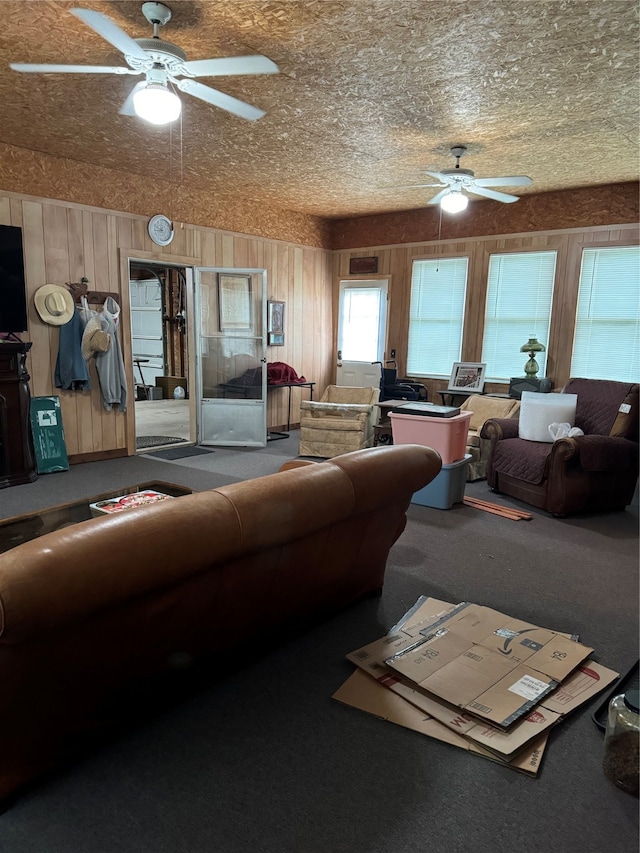 living room with ceiling fan, carpet floors, wood walls, and a textured ceiling