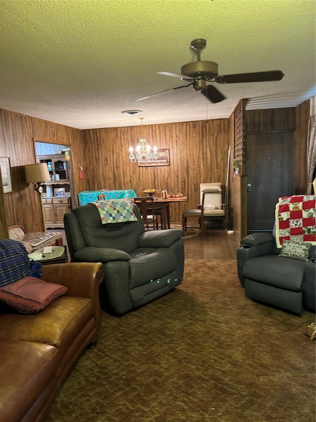 living room with ceiling fan with notable chandelier, dark colored carpet, wood walls, and a textured ceiling