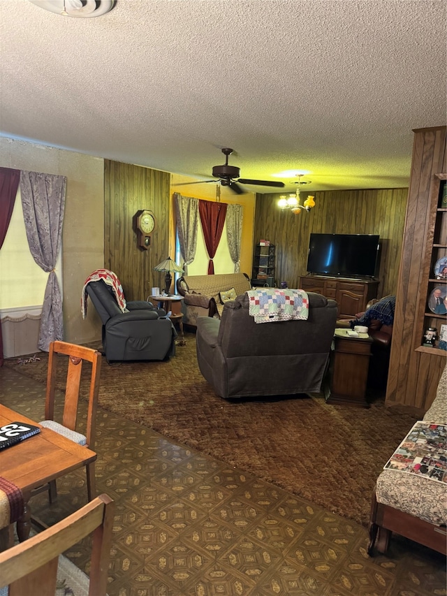 living room featuring ceiling fan with notable chandelier, wooden walls, a textured ceiling, and dark carpet