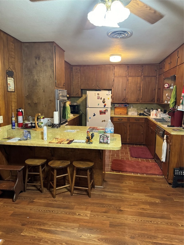 kitchen featuring dark hardwood / wood-style floors, kitchen peninsula, a kitchen bar, white fridge, and stainless steel oven