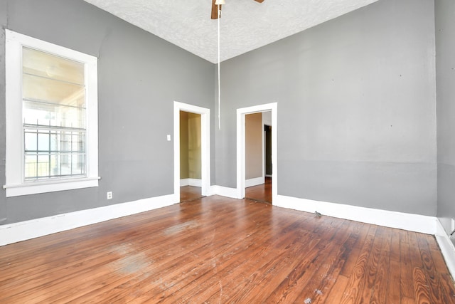 spare room featuring wood-type flooring, vaulted ceiling, a textured ceiling, and ceiling fan