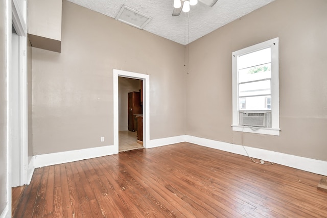 empty room featuring a textured ceiling, wood-type flooring, ceiling fan, and cooling unit