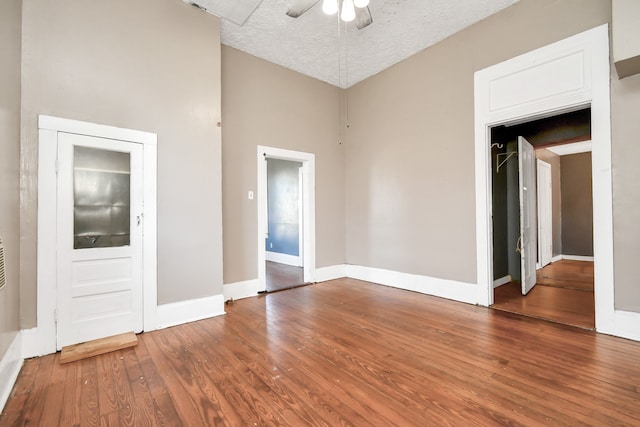 unfurnished room with wood-type flooring, a textured ceiling, a towering ceiling, and ceiling fan