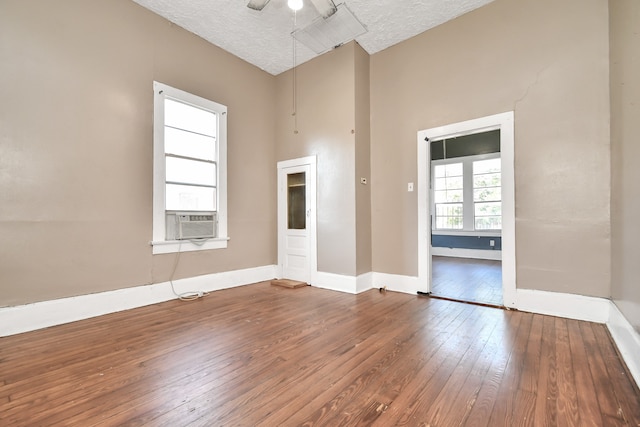 empty room with ceiling fan, cooling unit, a textured ceiling, and hardwood / wood-style flooring