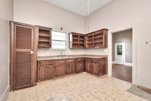 kitchen with a textured ceiling, dark brown cabinetry, a high ceiling, and sink