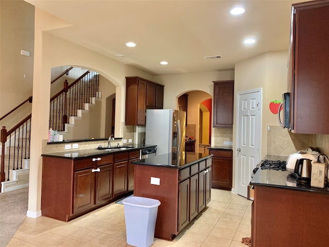 kitchen featuring light tile patterned flooring, sink, tasteful backsplash, a kitchen island, and appliances with stainless steel finishes