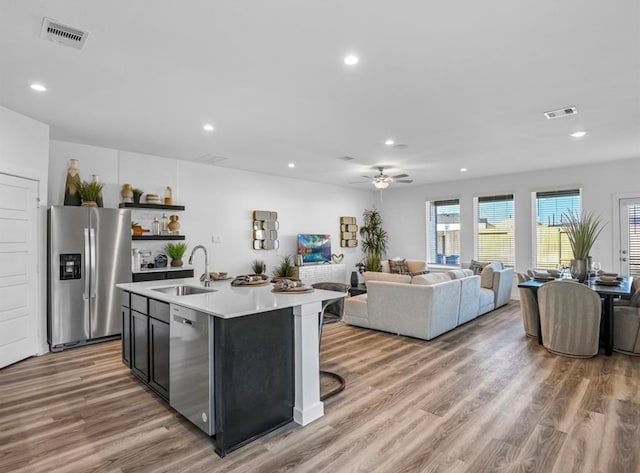 kitchen with stainless steel appliances, light wood-type flooring, ceiling fan, a kitchen island with sink, and sink