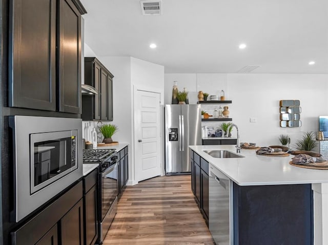 kitchen with sink, dark brown cabinets, a kitchen island with sink, stainless steel appliances, and dark hardwood / wood-style floors