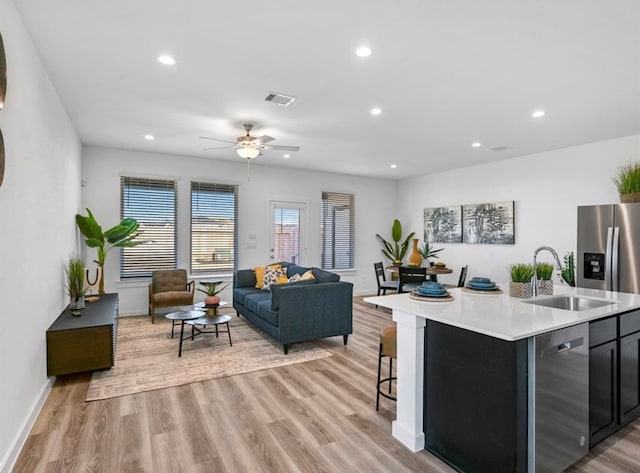 kitchen with ceiling fan, an island with sink, sink, light hardwood / wood-style flooring, and dishwasher