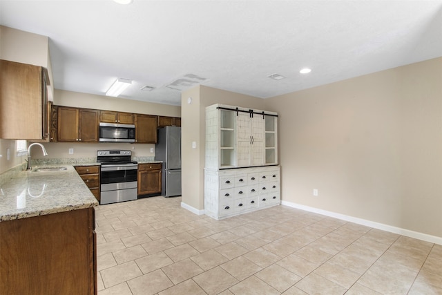 kitchen with light stone counters, light tile patterned flooring, sink, appliances with stainless steel finishes, and a barn door