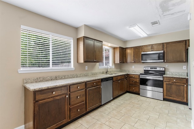 kitchen with light stone countertops, stainless steel appliances, dark brown cabinetry, and sink