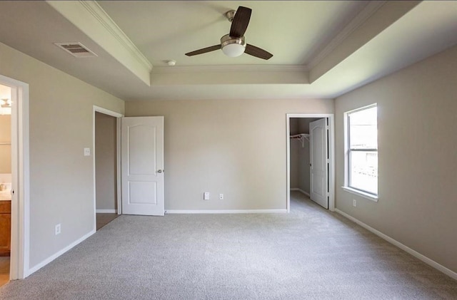 unfurnished bedroom featuring light colored carpet, a raised ceiling, ensuite bath, and ornamental molding