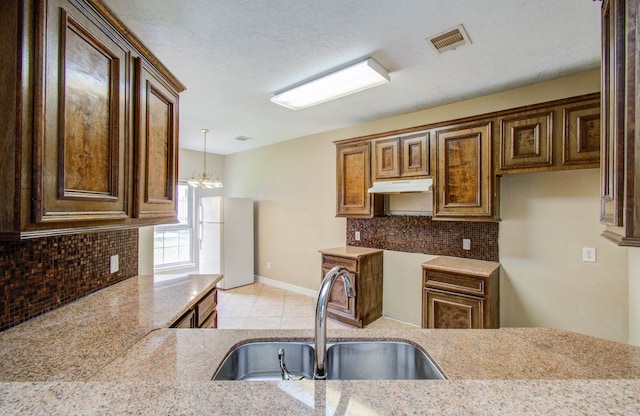 kitchen featuring light tile patterned flooring, backsplash, white fridge, sink, and a chandelier