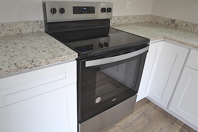 kitchen with wood-type flooring, electric range, light stone counters, and white cabinets