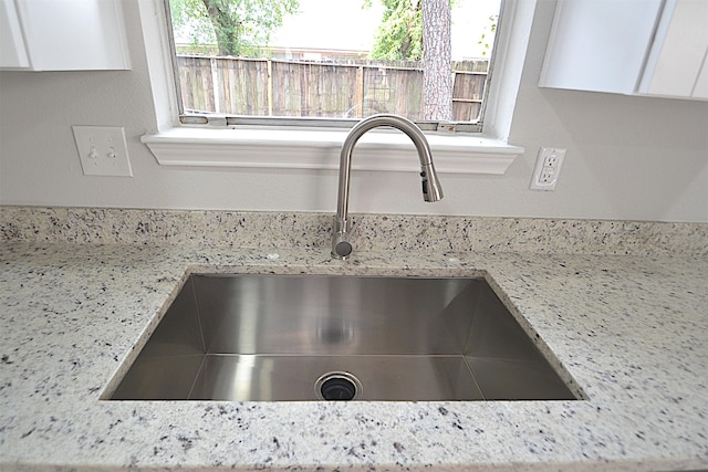 room details with light stone countertops, sink, and white cabinetry