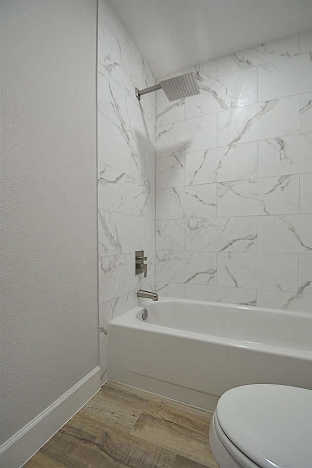 bathroom with wood-type flooring, tiled shower / bath combo, and toilet