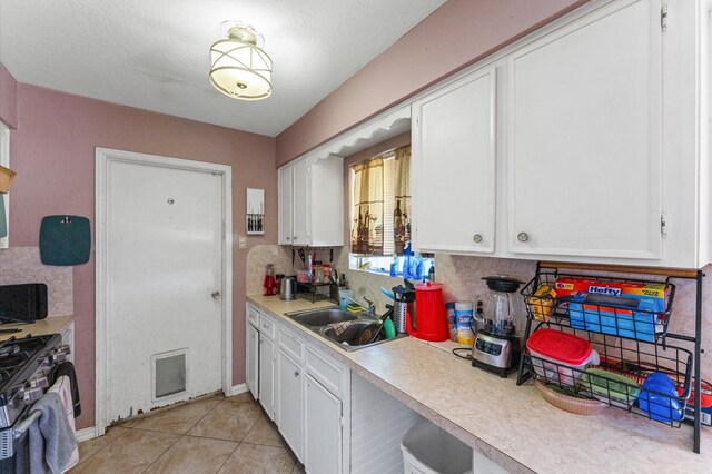 kitchen with tasteful backsplash, sink, white cabinets, gas range, and light tile patterned floors