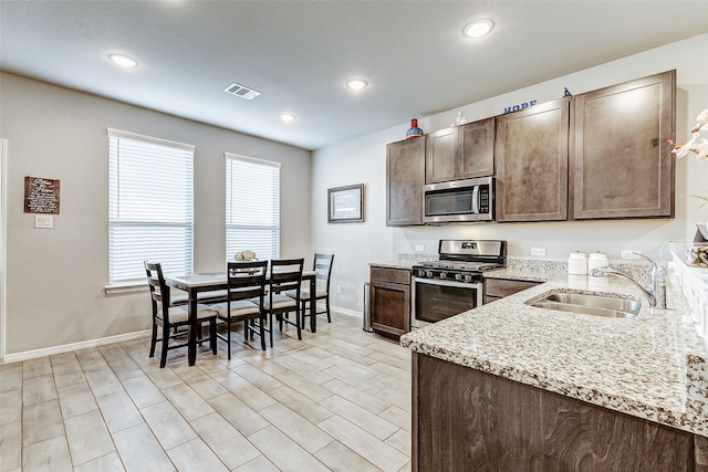 kitchen with light stone counters, stainless steel appliances, light hardwood / wood-style flooring, dark brown cabinetry, and sink