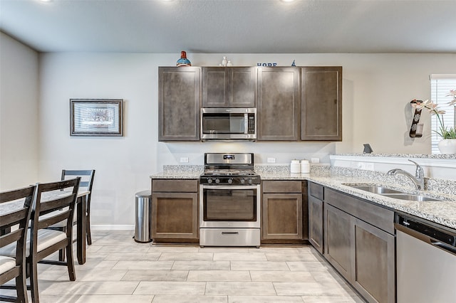 kitchen with light stone countertops, stainless steel appliances, dark brown cabinetry, and sink