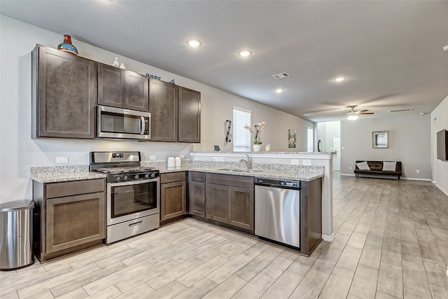 kitchen with ceiling fan, sink, kitchen peninsula, stainless steel appliances, and light wood-type flooring