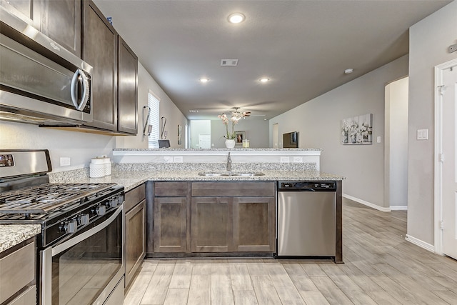 kitchen with appliances with stainless steel finishes, kitchen peninsula, light stone countertops, light wood-type flooring, and sink