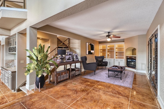 living room featuring ceiling fan, a textured ceiling, built in features, dark tile patterned flooring, and sink