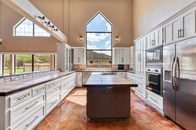 kitchen with a center island, appliances with stainless steel finishes, tile counters, and a towering ceiling