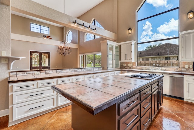 kitchen featuring decorative backsplash, white cabinets, tile counters, and a towering ceiling