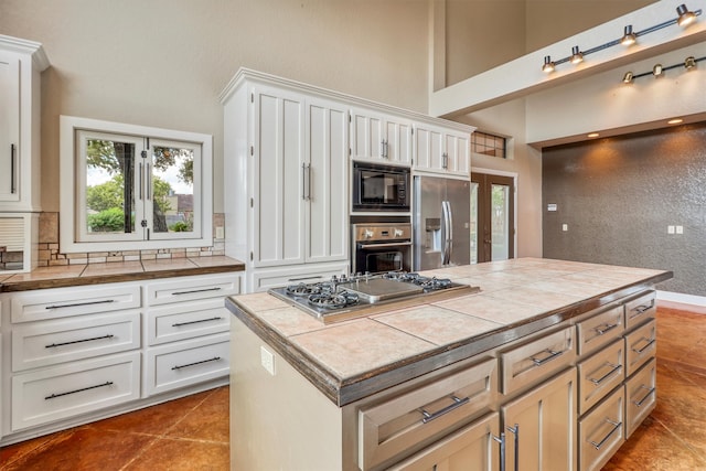 kitchen featuring tile countertops, a kitchen island, appliances with stainless steel finishes, and white cabinetry