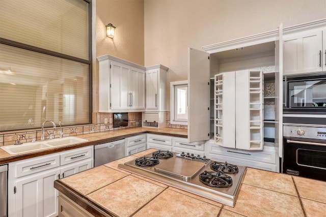 kitchen with tile countertops, stainless steel appliances, sink, white cabinets, and tasteful backsplash