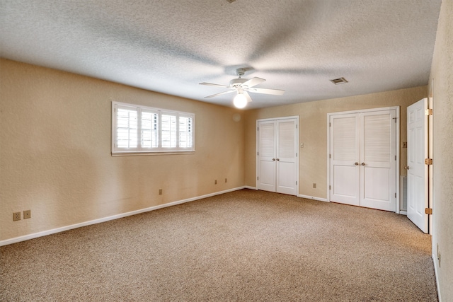 unfurnished bedroom with multiple closets, a textured ceiling, carpet floors, and ceiling fan