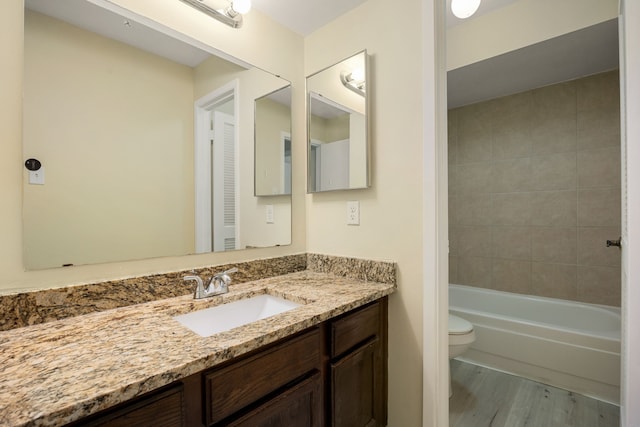 full bathroom with vanity, tiled shower / bath, hardwood / wood-style floors, and toilet