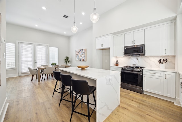 kitchen featuring white cabinets, light stone counters, stove, and a center island