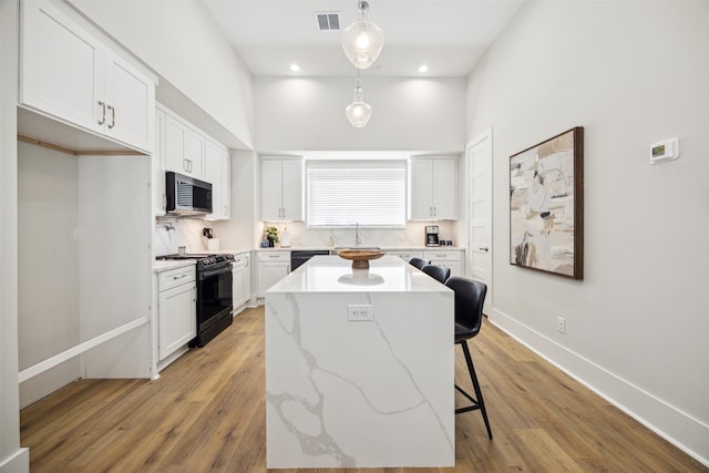 kitchen featuring a kitchen island, black appliances, white cabinetry, and pendant lighting