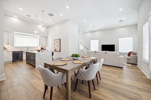 dining area featuring a wealth of natural light, a towering ceiling, light wood-type flooring, and sink