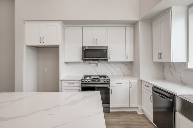 kitchen with white cabinetry, decorative backsplash, light hardwood / wood-style flooring, appliances with stainless steel finishes, and light stone countertops